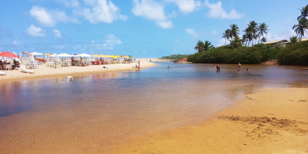 Água cristalina de Imbassaí com pessoas se banhando