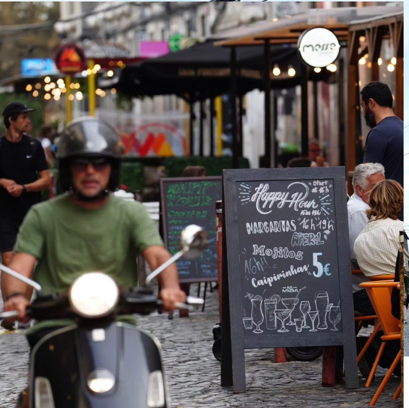 Rua com bares do LX Factory e uma pessoa andando de moto. Lisboa, Portugal