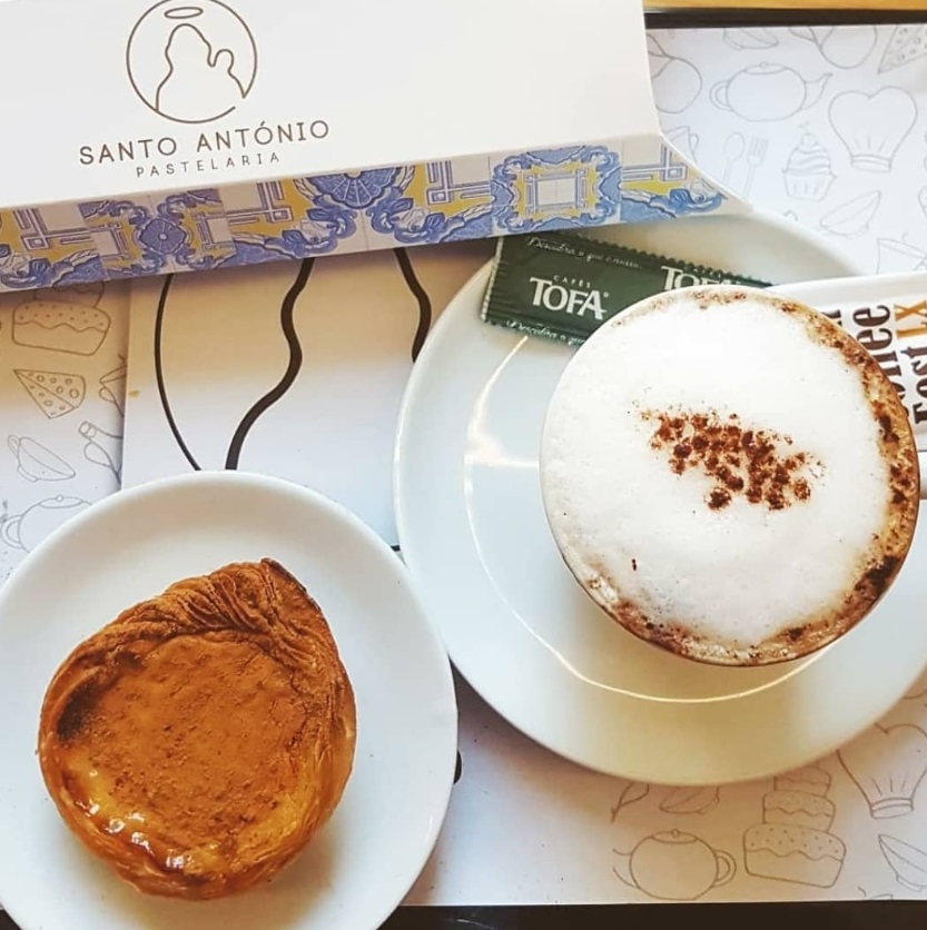 Pastel de nata no prato, um café com leite na chícara e uma caixa de embalagem da Pastelaria Santo Antonio, Lisboa, Portugal.