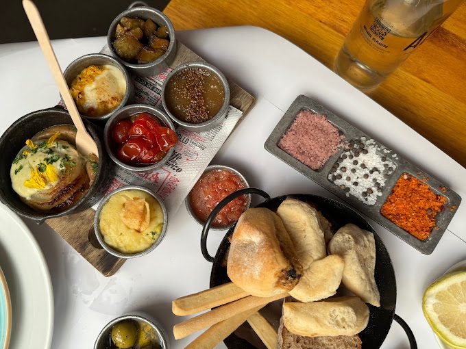 Mesa com pequenos potes de condimentos e acompanhamentos para comer com pão