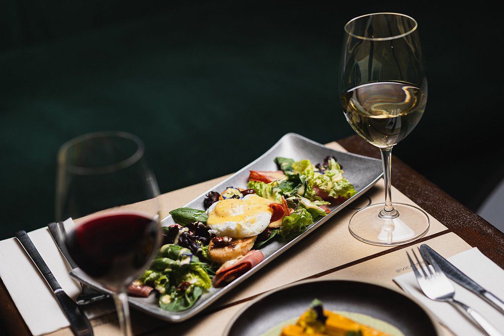 Mesa posta com duas taças de vinho tinto e um prato de legumes e verduras