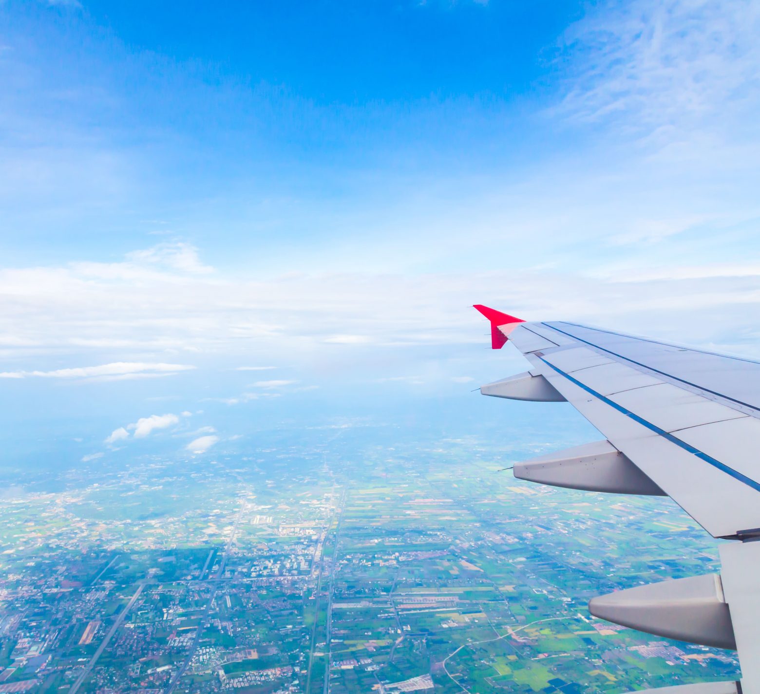 Asa de avião no céu e cidade embaixo.