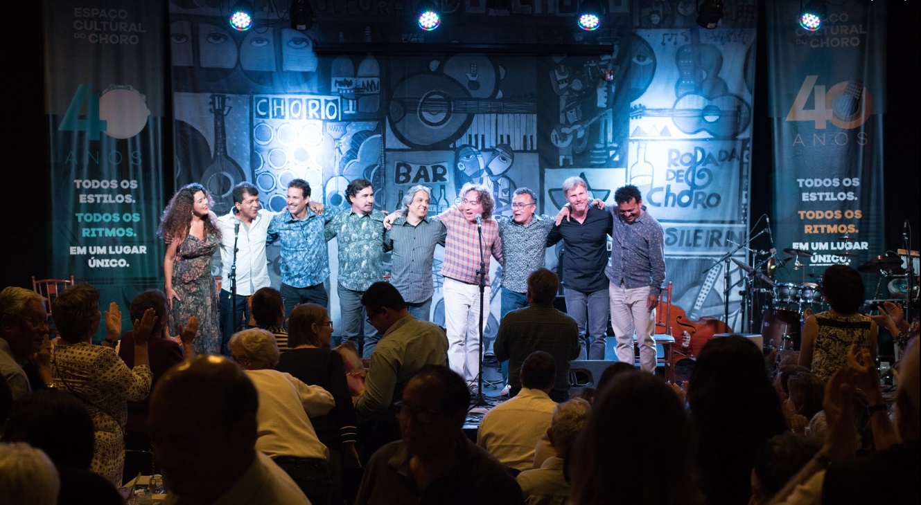 Artistas no palco do Clube do Choro, Brasília . Plateia de pé aplaudindo.