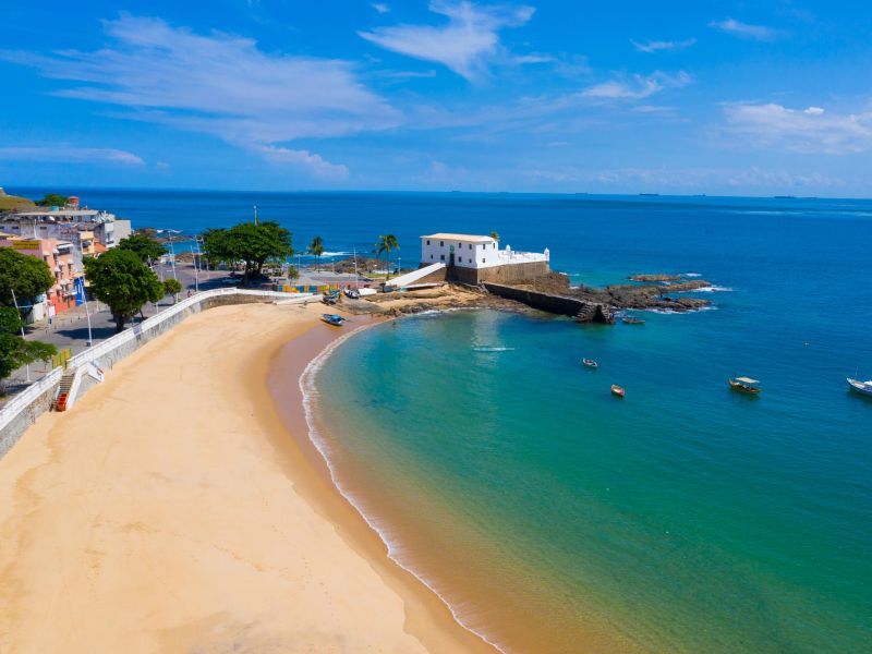 Praia do Porto da Barra - Salvador, Bahia - Imagem mostra areia da praia com ponto turístico atrás.