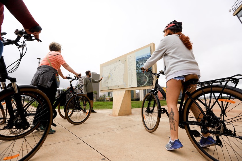 Turistas de bicicleta com guia vendo placa de Brasília