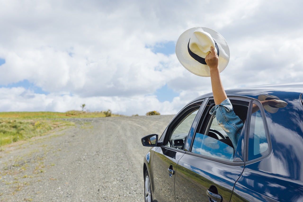 Carro n a estrada e mão segurando um chapéu n a janela