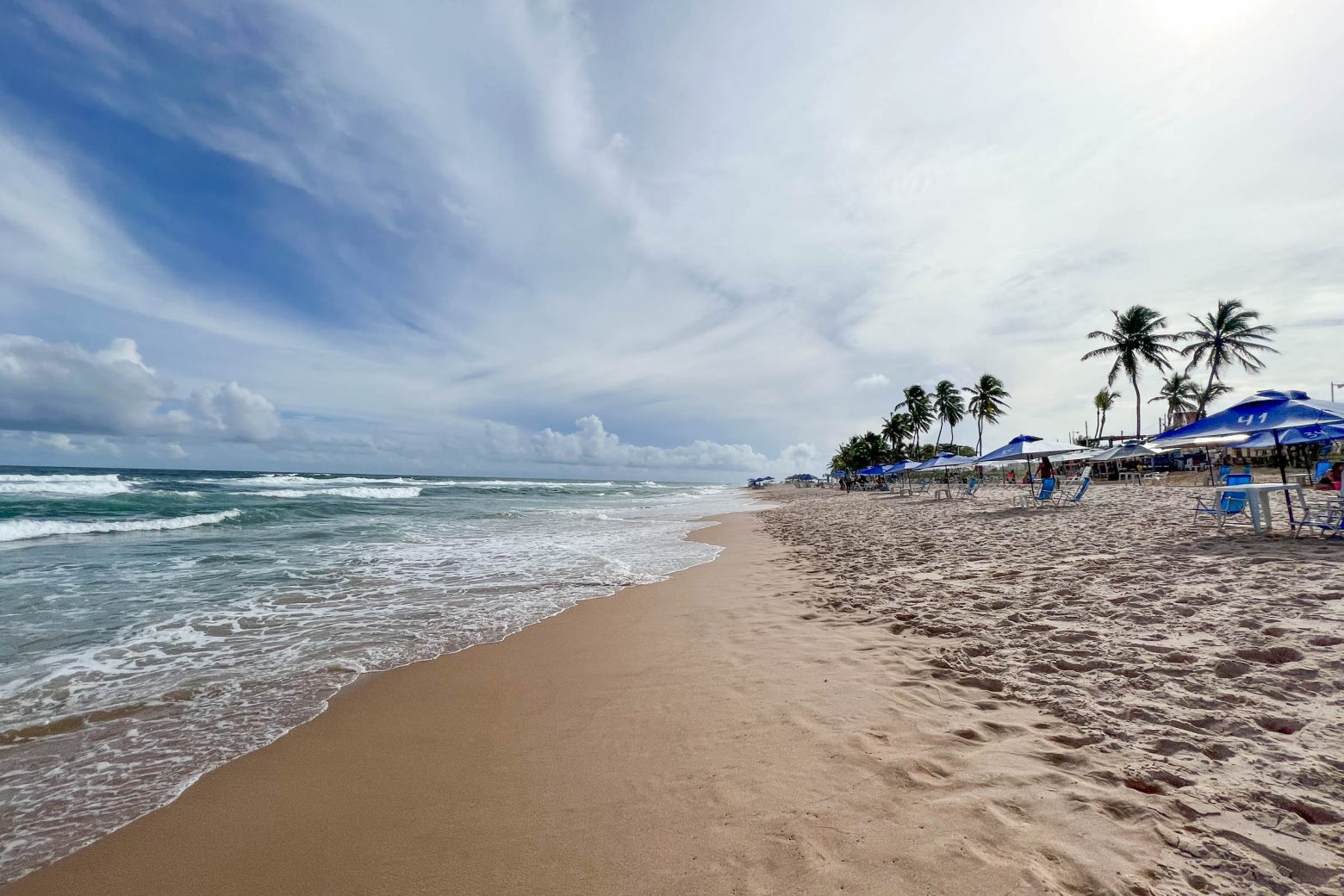 Praia de Stella Maris em Salvador, BA - Na imagem mostra o mar na lateral e areia a frente com coqueiros a vista.