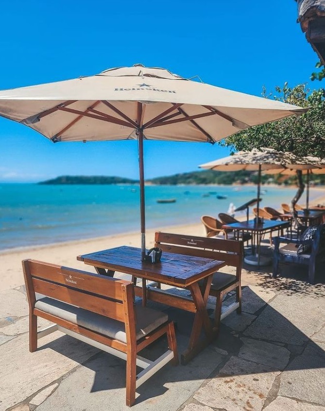 Mesa, guarda-sol e cadeira de um restaurante na beria da praia no Porto da BArra, Búzios