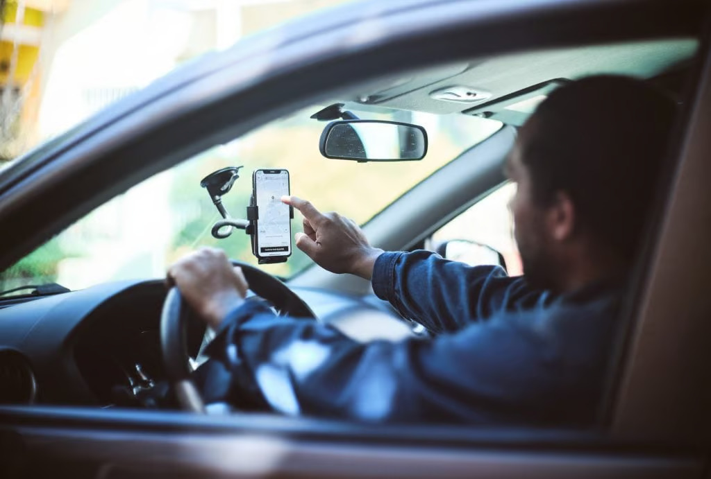 Motorista por aplicativo em carro mexendo no celular