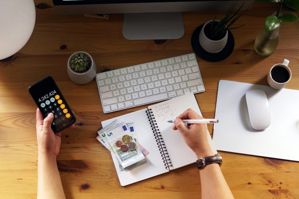 Pessoa com calculadora, moedas, dinheiro, teclado, caderno e caneta na mão