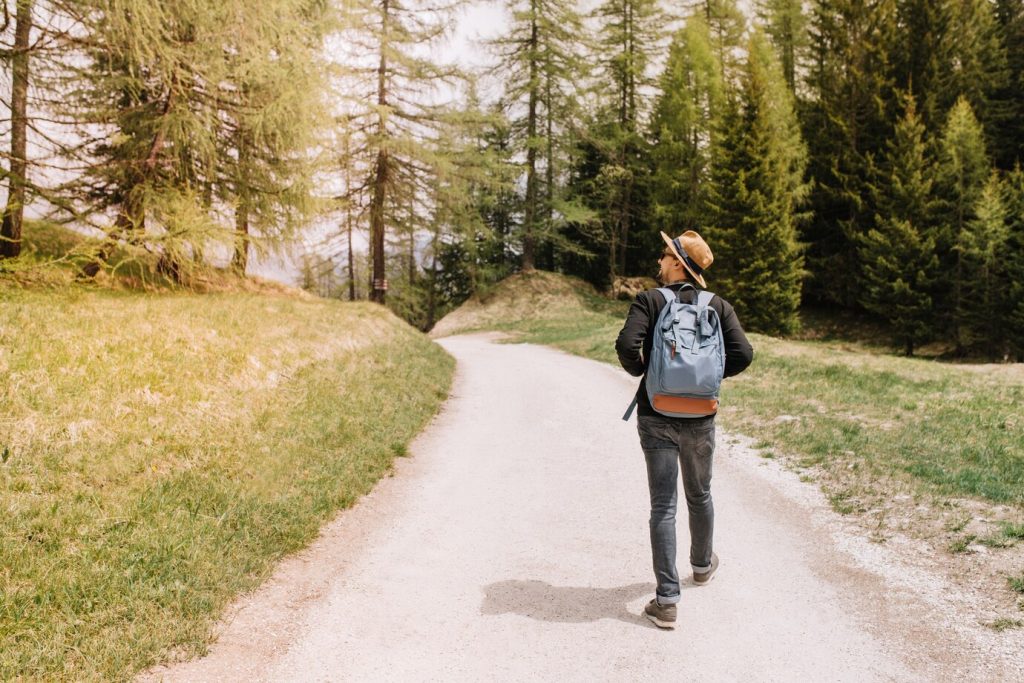 Homem andando numa trilha, com mochila e chapéu