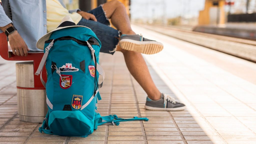 Viajante sentado esperando um trem. Mochila no chão. 